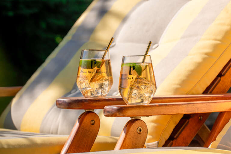 Twee glazen met een cocktail op basis van Pineau Des Charentes op de leuning van een strandstoel in de zon