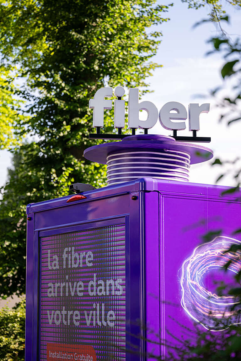 Vue rapprochée du toit du van Proximus avec le logo "fiber" et l’inscription "La fibre arrive dans votre ville".