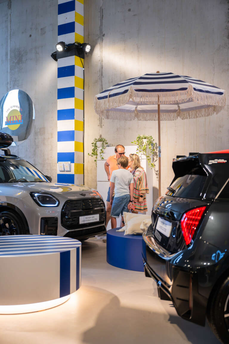 Visiteurs discutant à l’ombre d’un parasol dans l’espace d’exposition MINI.