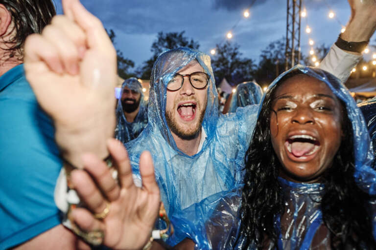 Festivalgangers dansen en zingen in de regen, gekleed in blauwe poncho's.