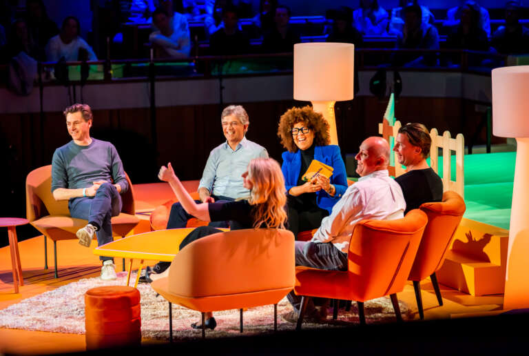 Round table discussion on stage in a warm and immersive setting, with speakers discussing in front of an audience