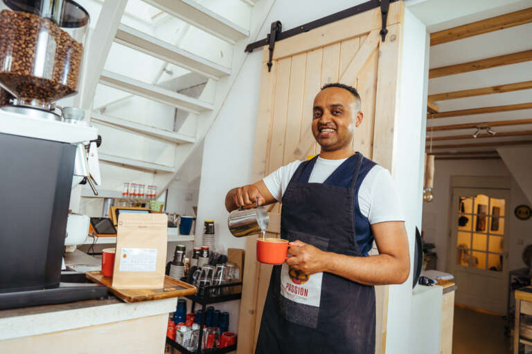 A barista pouring milk into a cup in a cozy coffee shop.