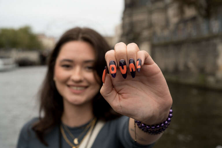 Young smiling employee proudly displaying a manicure with the letters OVAL, a symbol of belonging to the agency